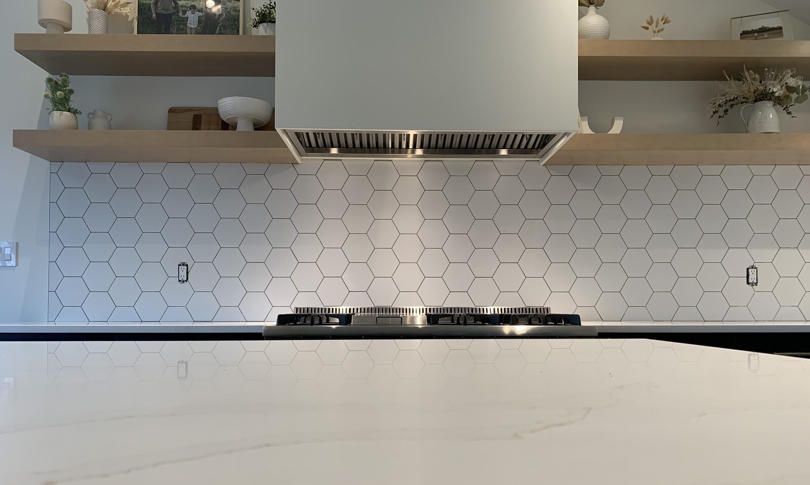 Hexagon tile backsplash behind a range hood with floating shelves