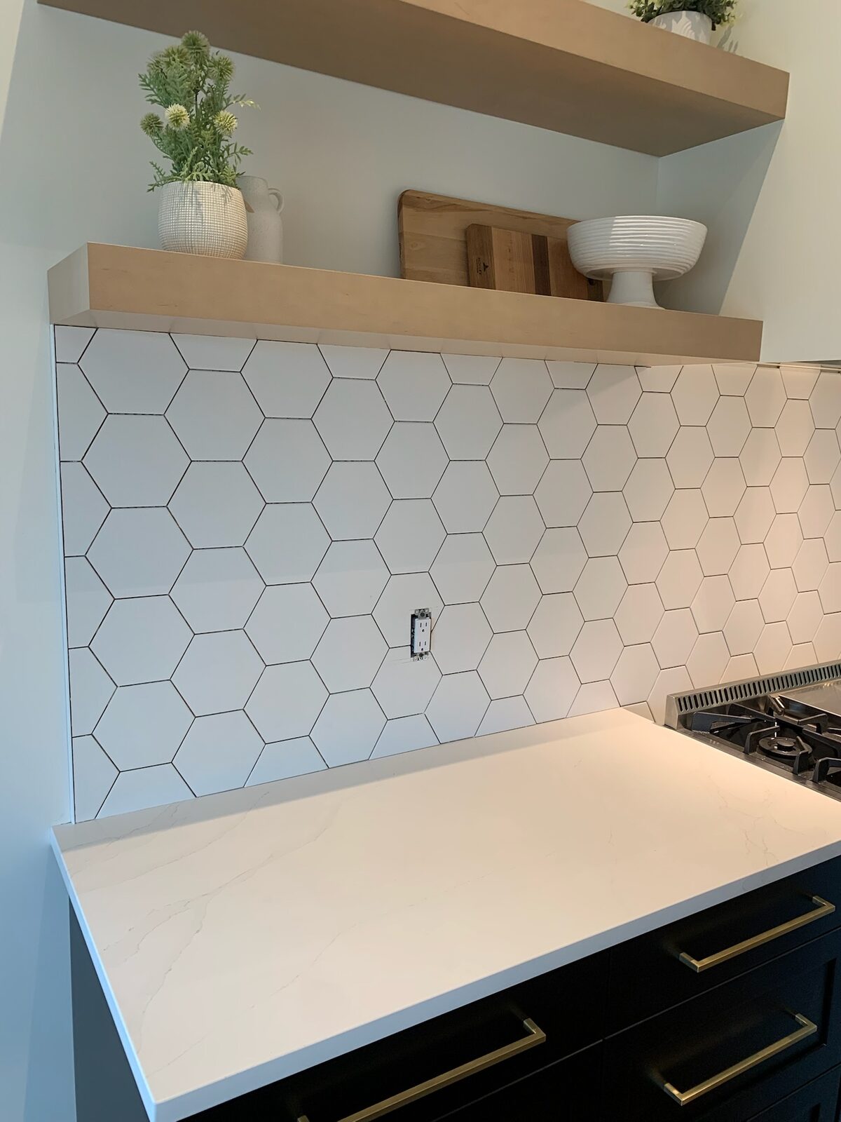 White hexagon tile backsplash with an oak floating shelf