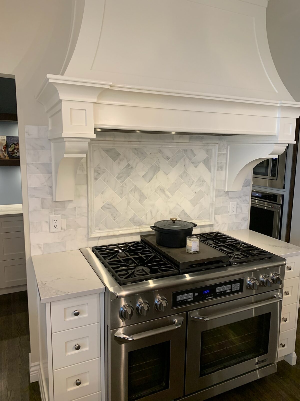 Marble herringbone backsplash behind a gas range and hood