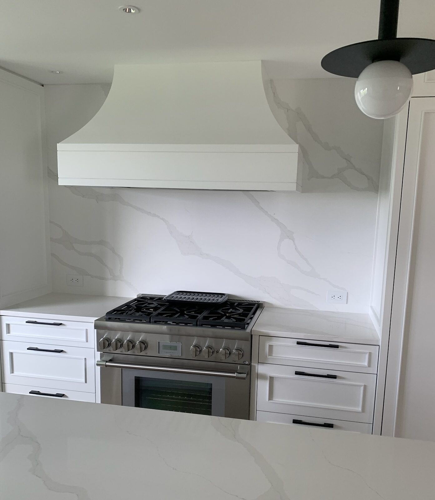Marble-look slab backsplash behind a range under a white hood