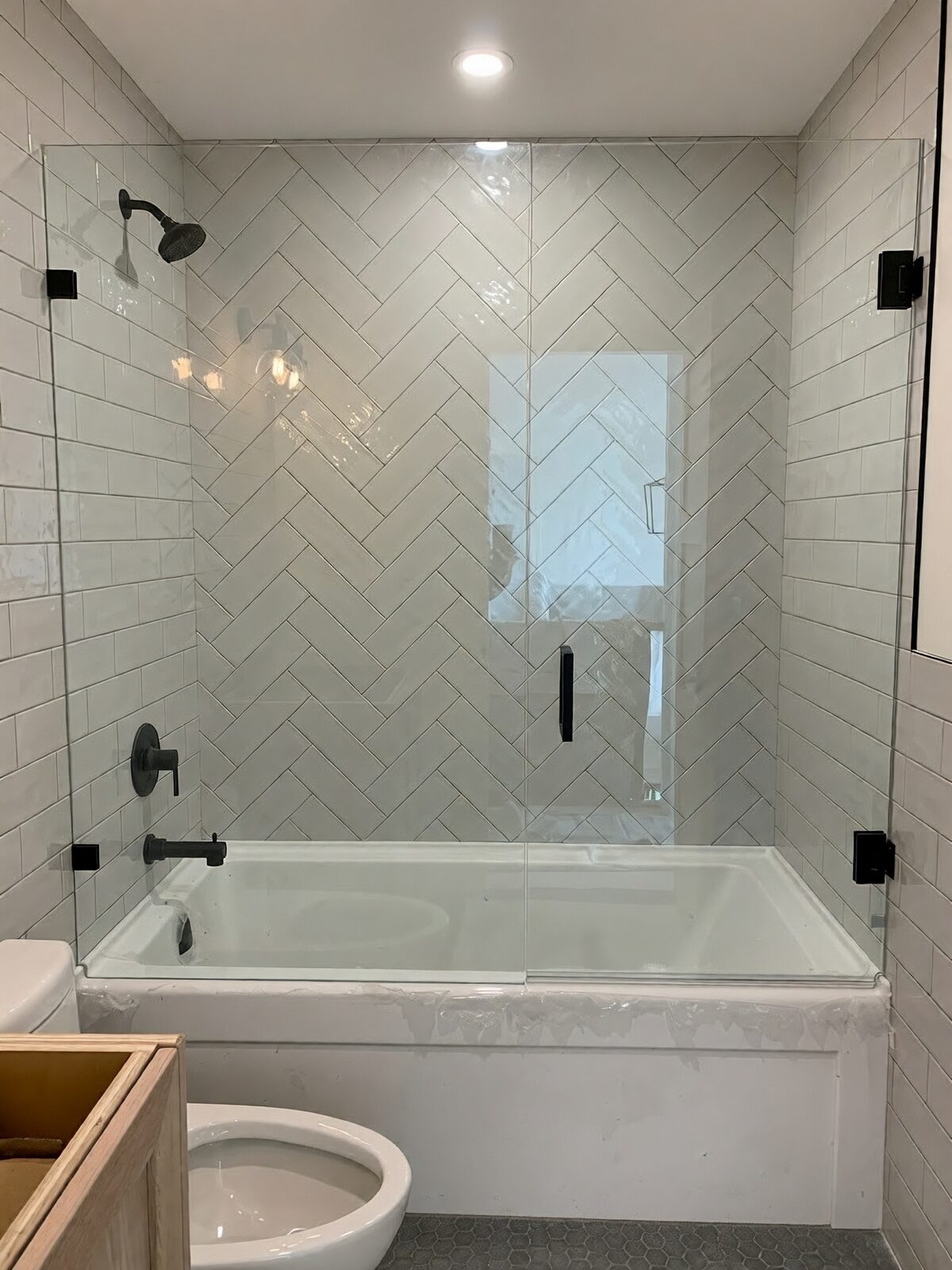 Glass panel over a drop-in tub with herringbone tile