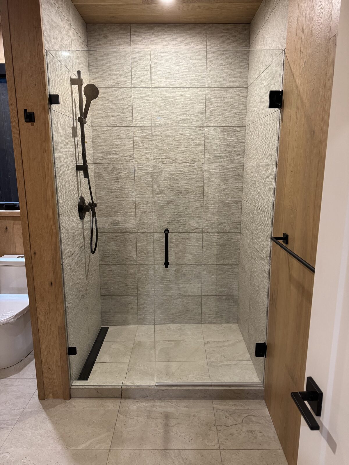 Frameless glass shower door in a wood-trimmed opening