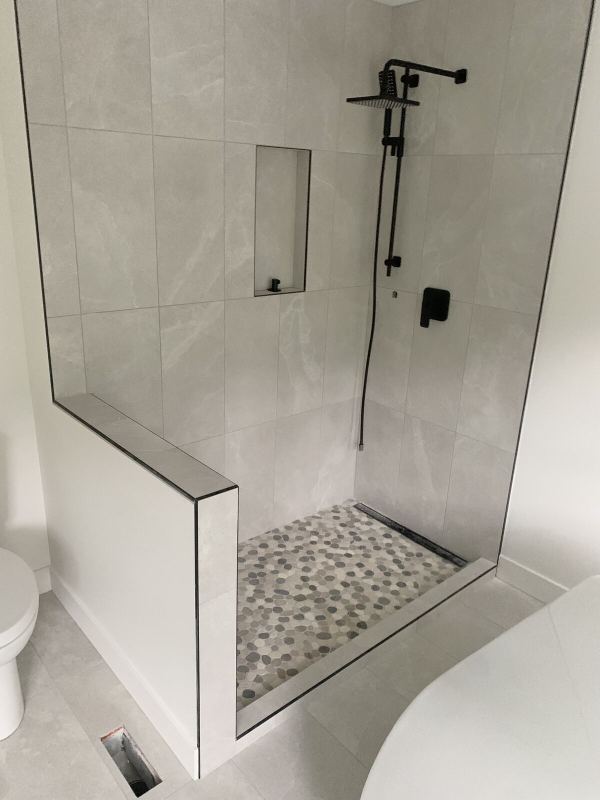 Shower with a pebble floor, niche and tiled half wall