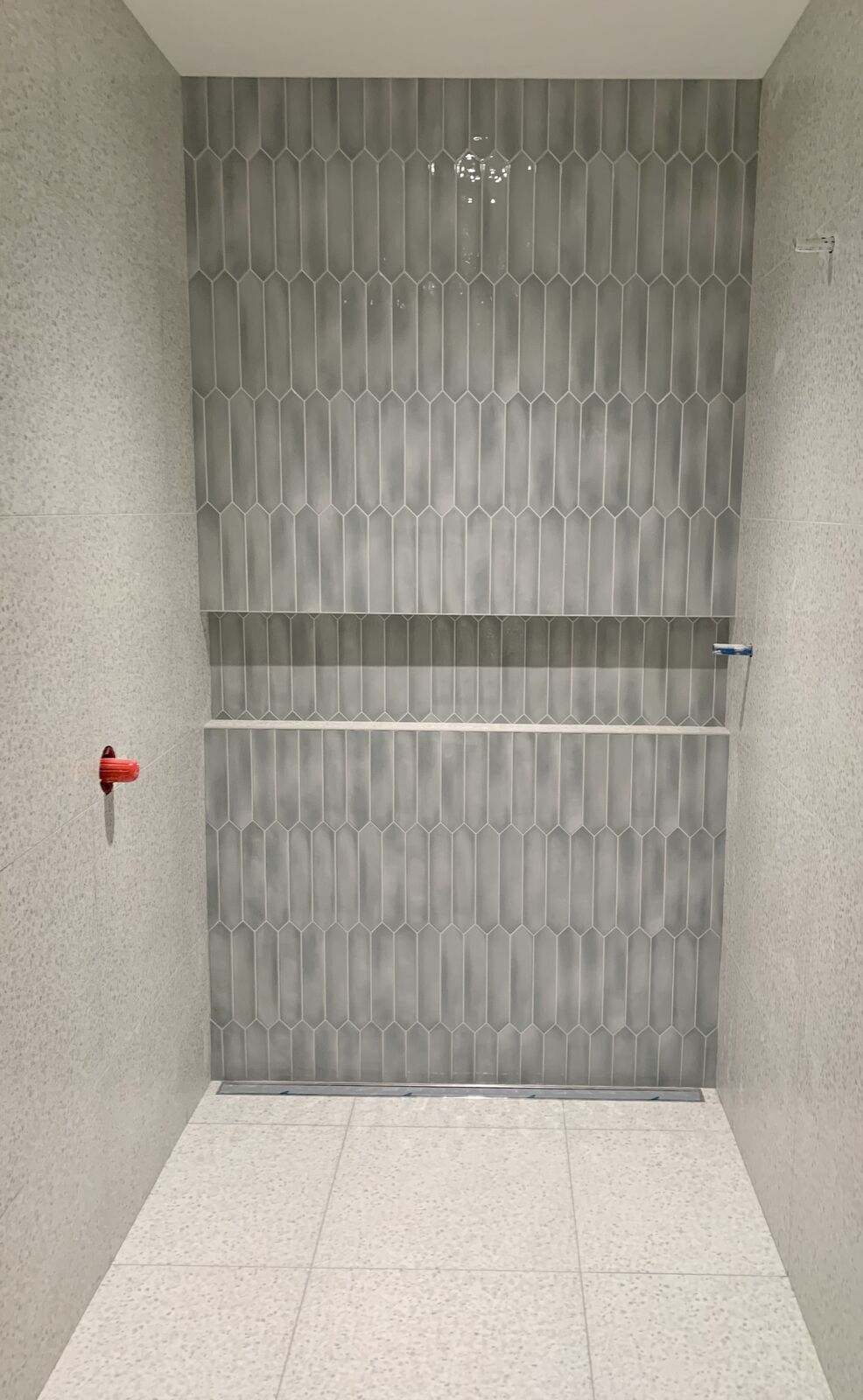 Shower with a green picket tile wall and terrazzo floor