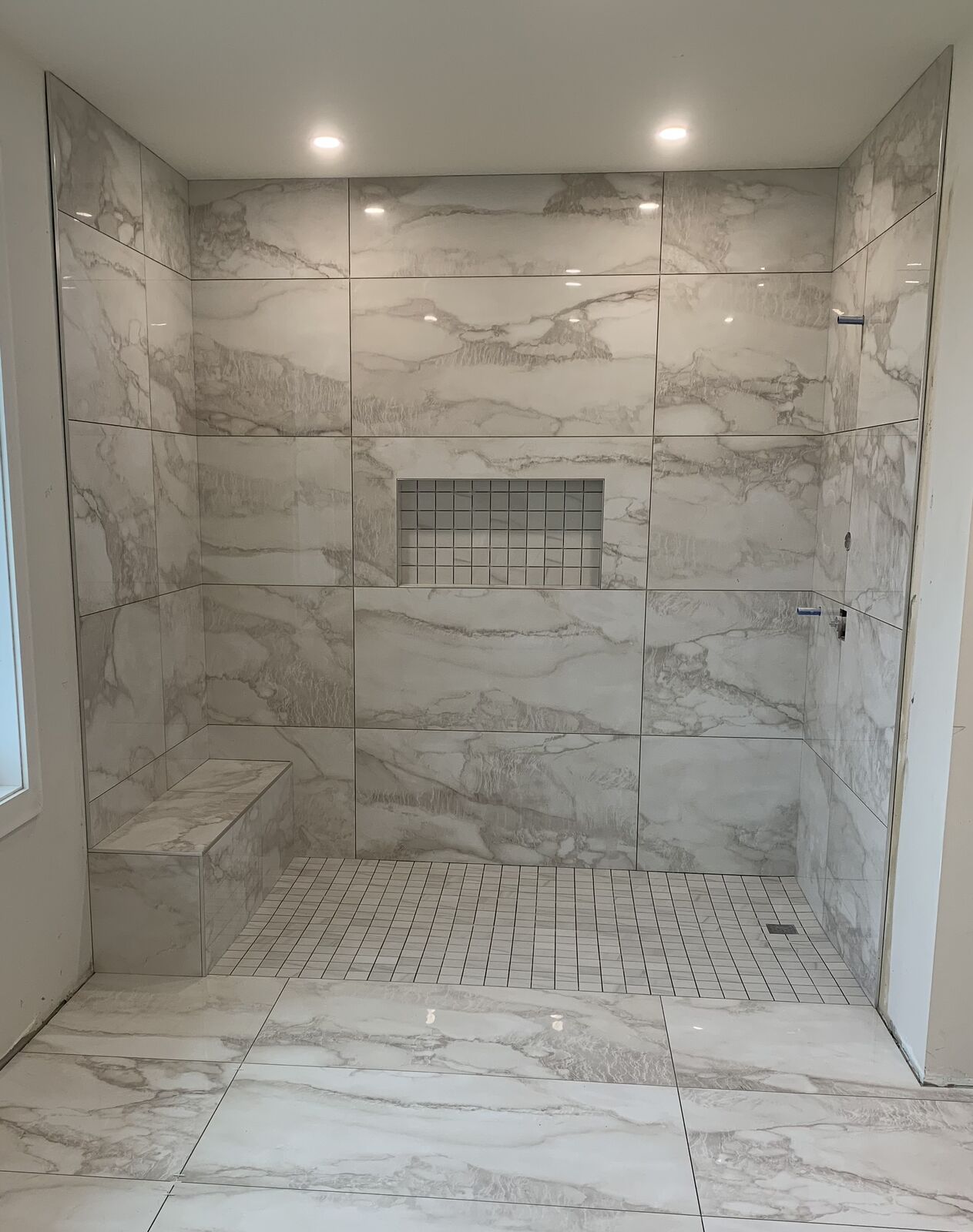 Large calacatta-look shower with a bench and mosaic niche